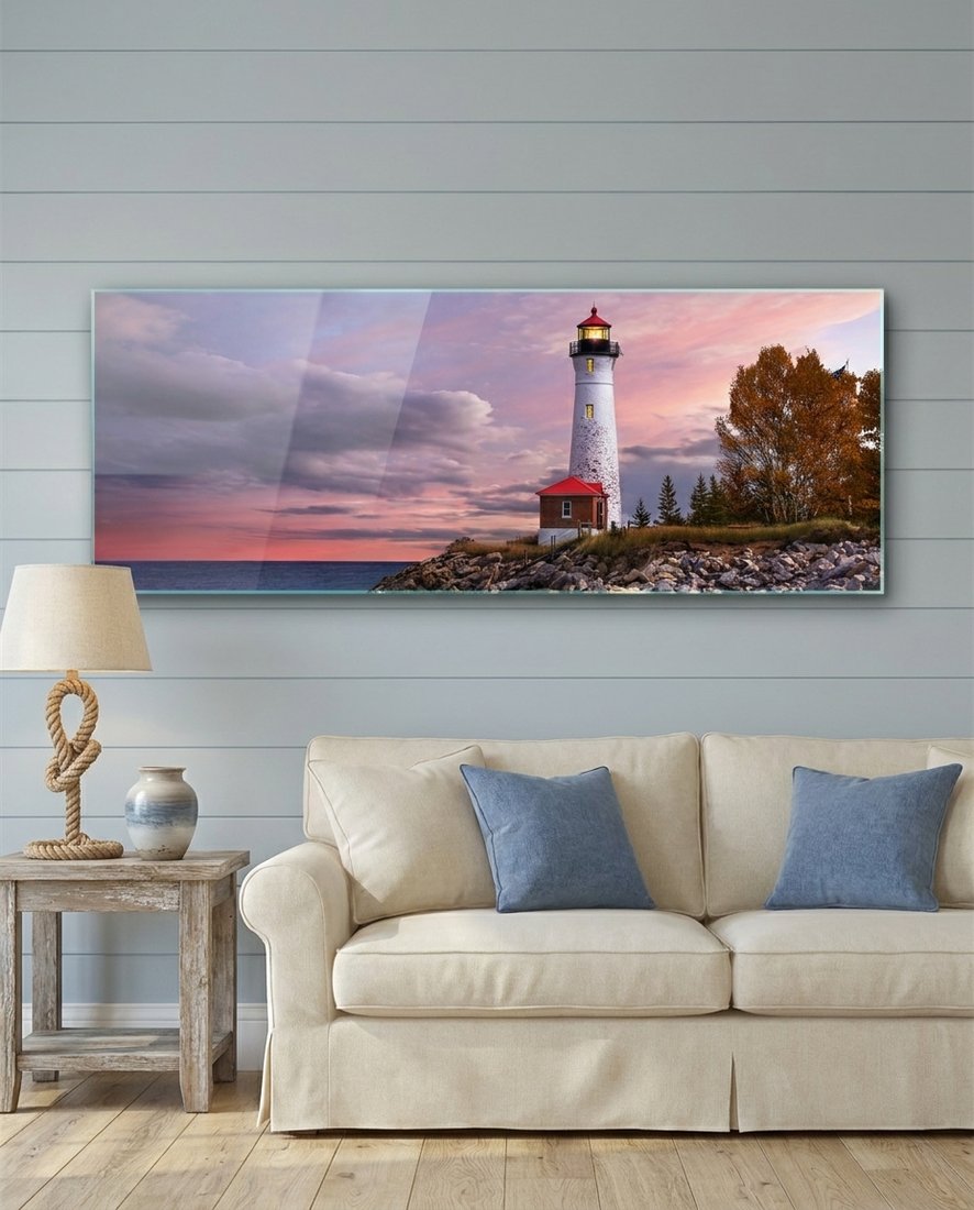 Lighthouse at dusk panoramic glass wall art above a cream sofa with blue cushions on a blue paneled wall