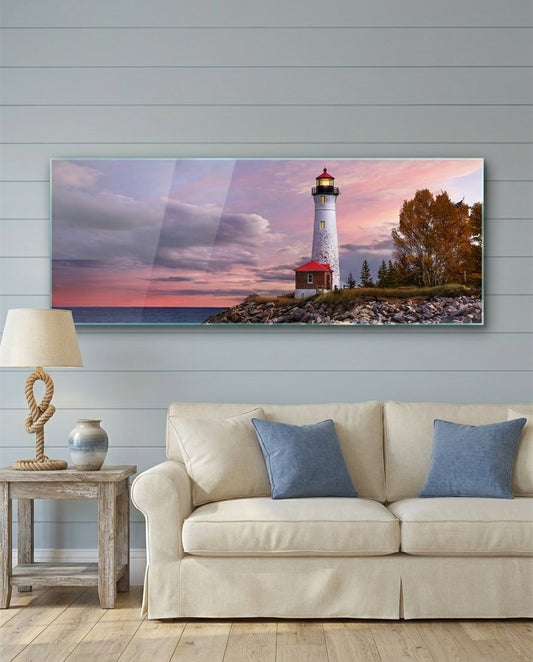 Lighthouse at dusk panoramic glass wall art above a cream sofa with blue cushions on a blue paneled wall