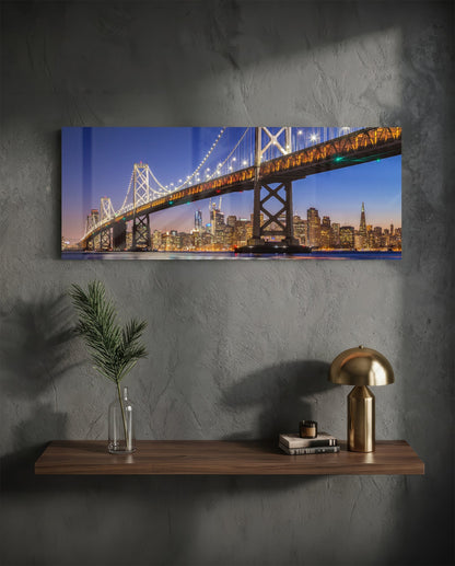 San Francisco Bay Bridge panoramic glass wall art on a dark wall above a shelf with a gold lamp