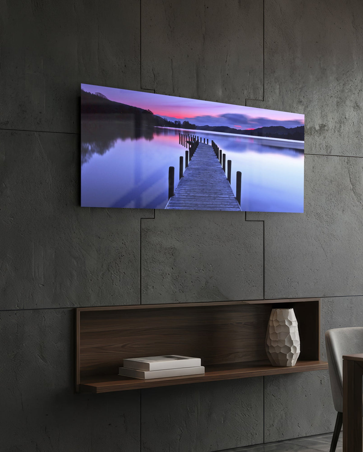 Purple twilight lake jetty glass wall art above a dark wood wall shelf on a charcoal paneled wall