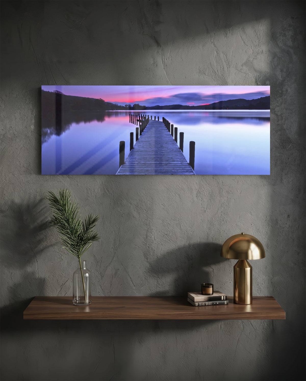 Purple twilight lake jetty glass wall art above a floating walnut shelf with a brass lamp