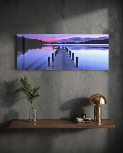 Purple twilight lake jetty glass wall art above a floating walnut shelf with a brass lamp