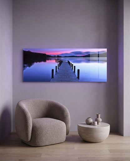 Purple twilight lake jetty panoramic glass wall art above a boucle armchair on a lilac wall