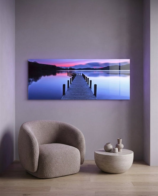 Purple twilight lake jetty panoramic glass wall art above a boucle armchair on a lilac wall