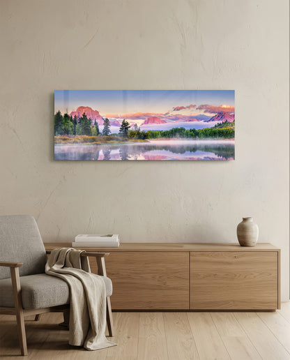 Pink dawn mountain lake panoramic glass wall art above a light wood sideboard beside a gray armchair