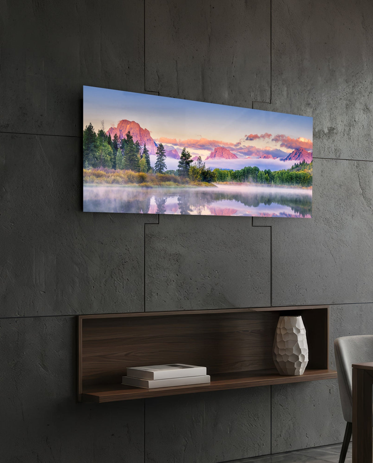 Pink dawn mountain lake panoramic glass wall art above a floating wood shelf on a dark stone wall