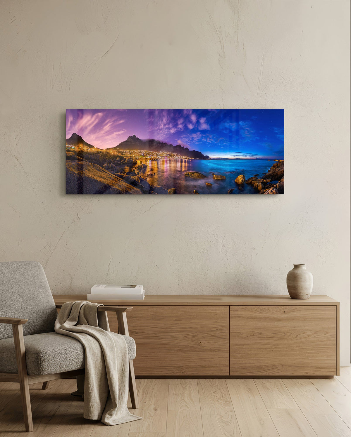 Coastal town at dusk panoramic glass wall art above a light wood sideboard and beige armchair