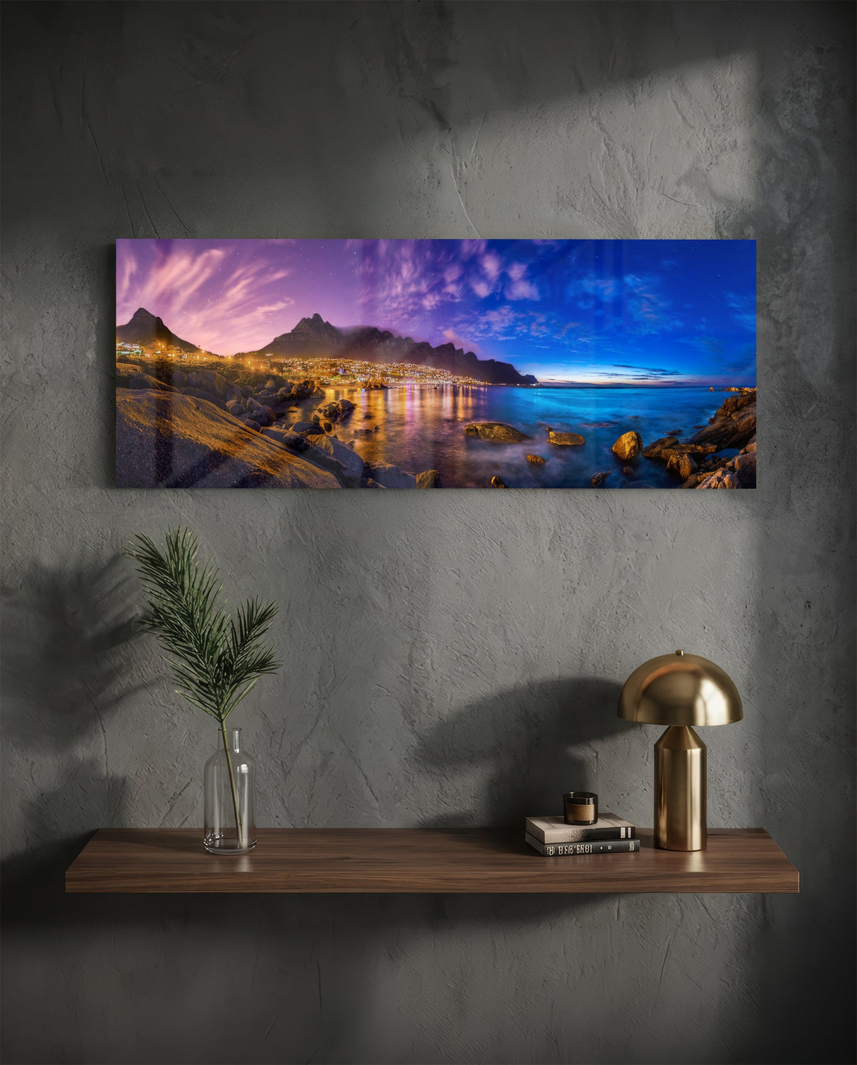Coastal town at dusk panoramic glass wall art on a dark wall above a shelf with a gold lamp