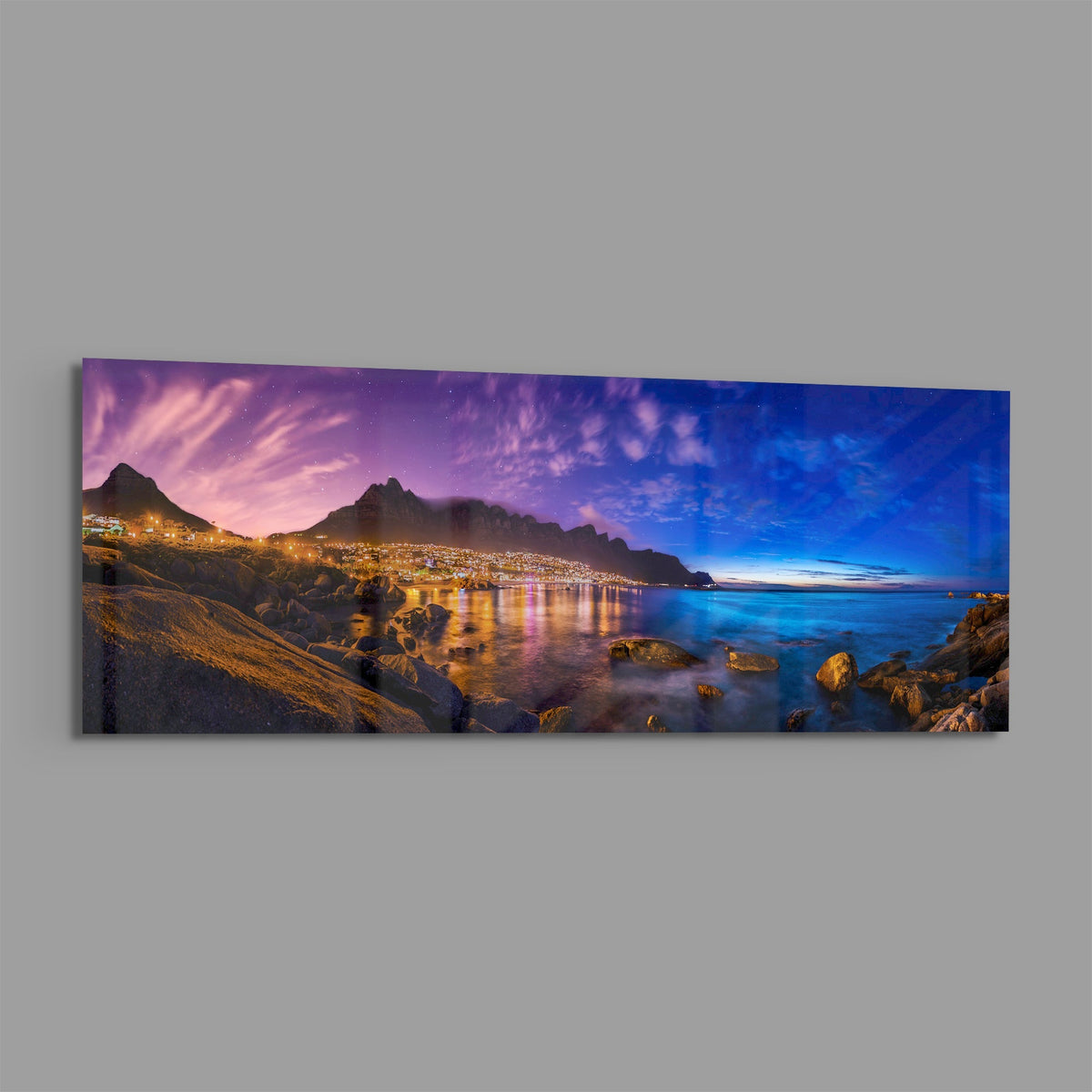 Coastal town at dusk panoramic glass wall art shown at an angle on a gray background