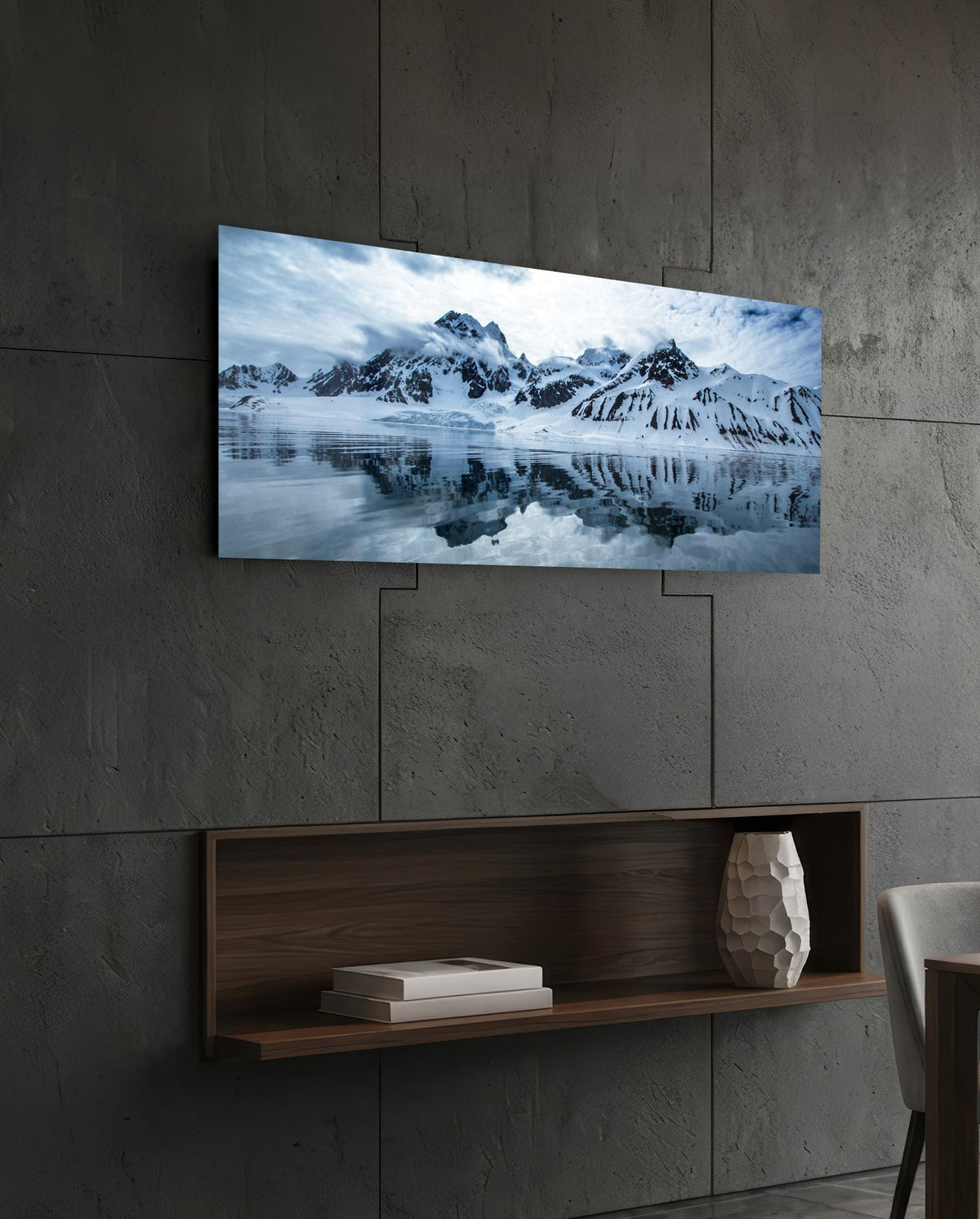 Snowy mountains icy lake panoramic glass wall art above a floating wood shelf on a dark stone wall