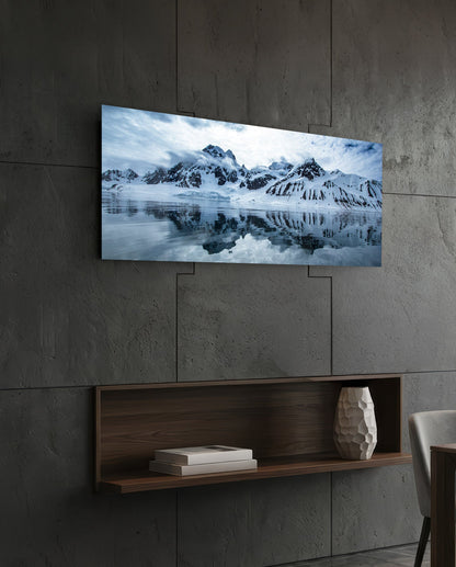 Snowy mountains icy lake panoramic glass wall art above a floating wood shelf on a dark stone wall