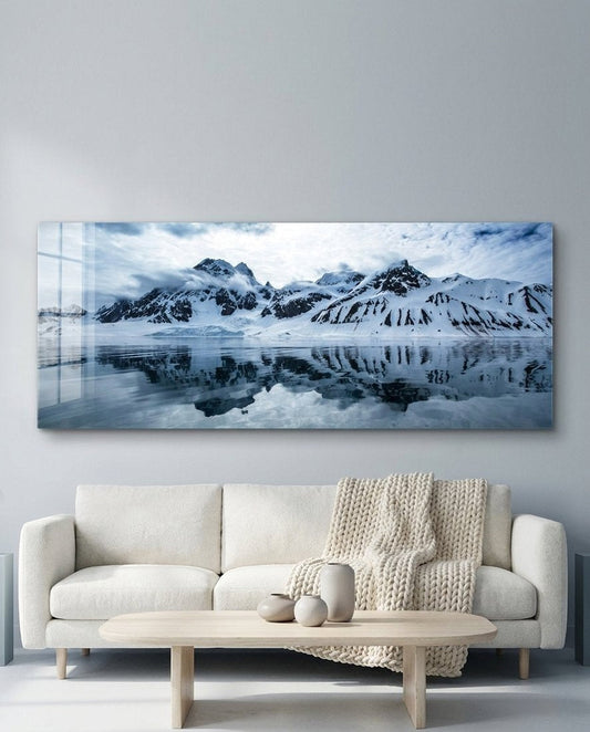 Snowy mountains icy lake panoramic glass wall art above a white sofa and an oval coffee table