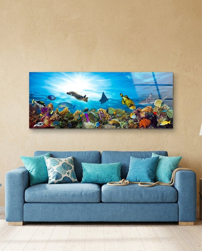 Coral reef sea turtle panoramic glass wall art above a blue sofa with teal cushions on a sand-colored wall