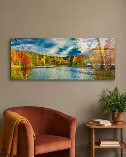 Autumn lake panoramic glass wall art above a rust armchair, a fern and a wooden side table with books