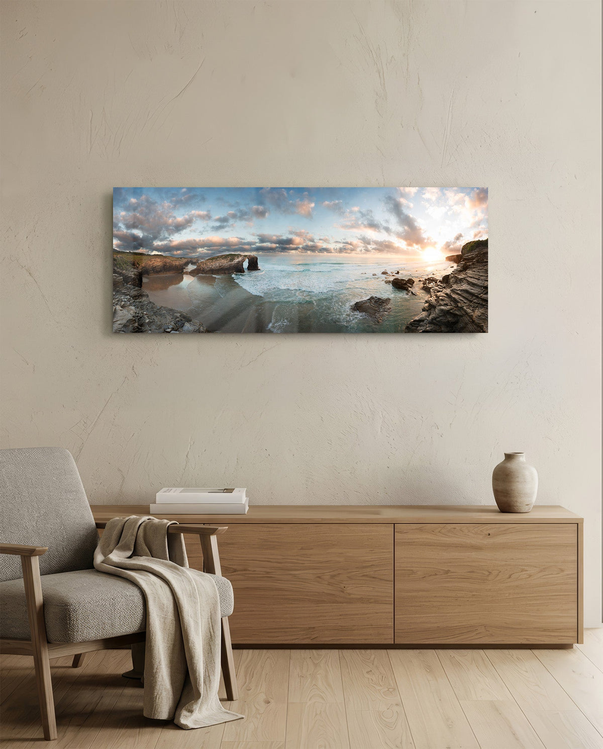 Rock arch coastline at sunset glass wall art above a light oak sideboard beside a cream armchair