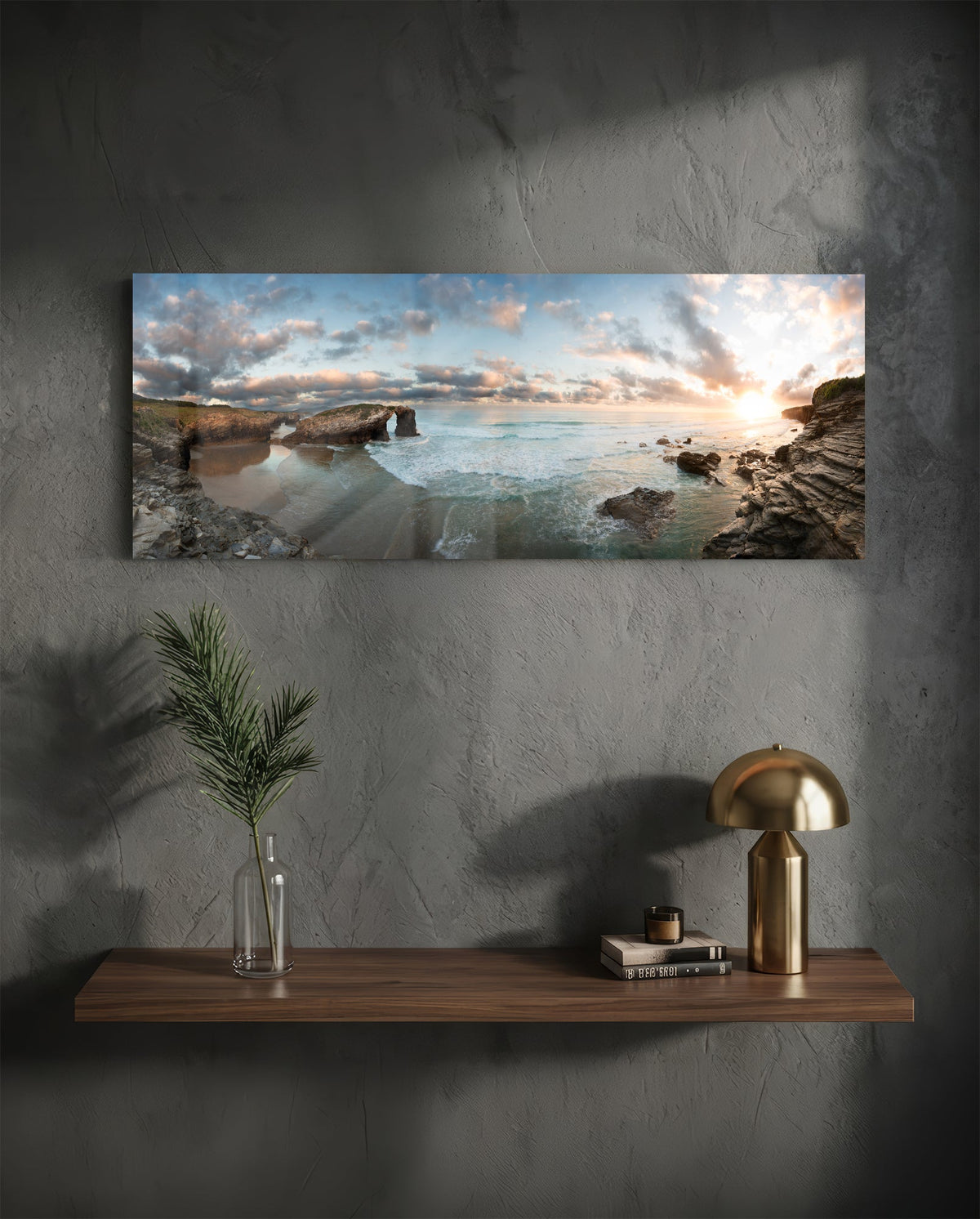 Rock arch coastline at sunset glass wall art above a floating walnut shelf with a brass lamp