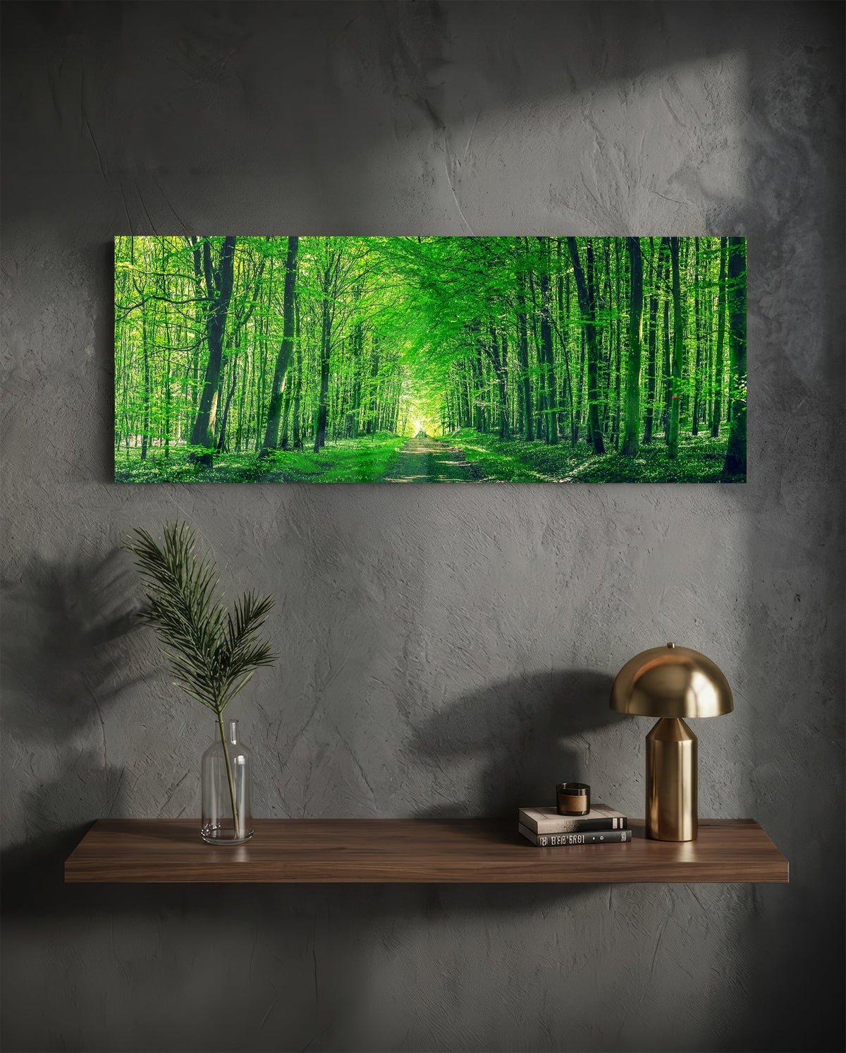 Green forest path glass wall art above a floating shelf with a brass lamp and a plant in a vase