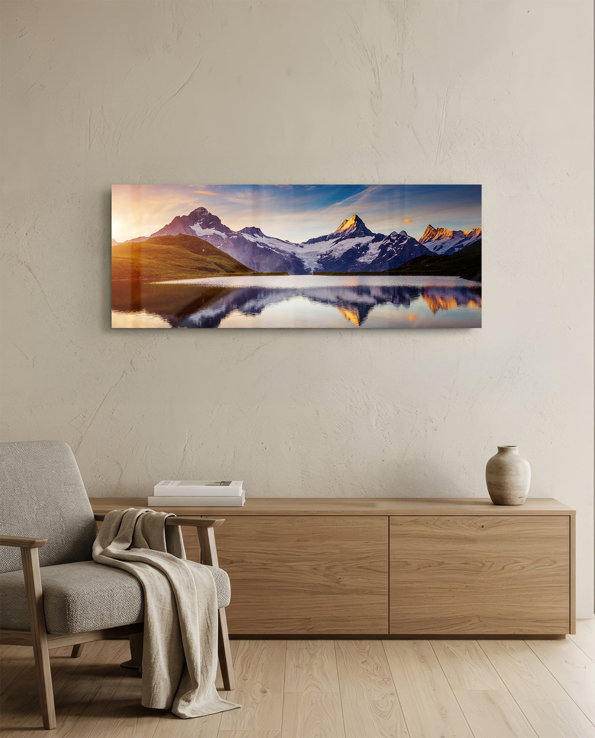 Sunrise alpine peaks lake panoramic glass wall art above a light wood sideboard beside a gray armchair