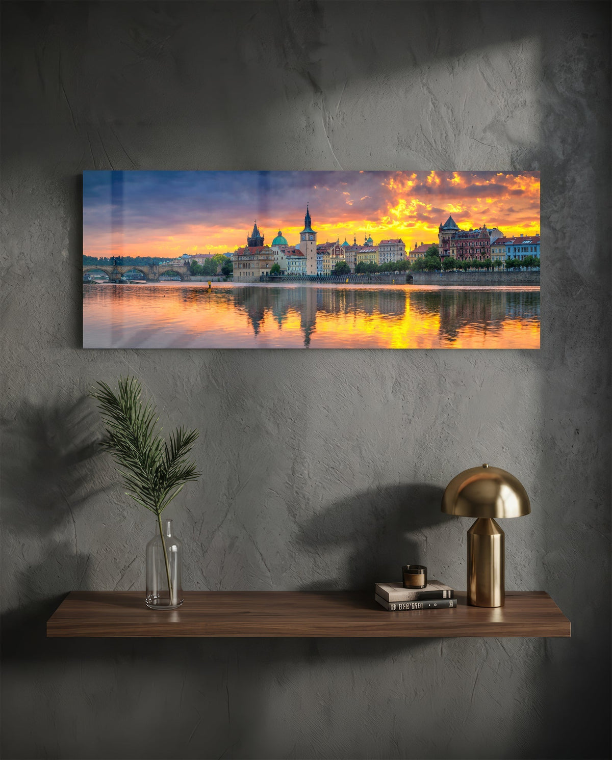 Prague riverside sunset panoramic glass wall art on a dark wall above a shelf with a gold lamp