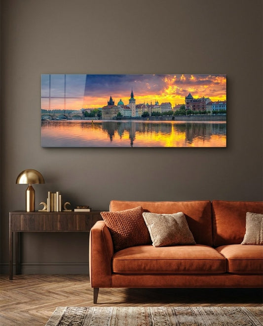 Prague riverside with spires and a stone bridge at sunset, panoramic glass wall art above a rust orange sofa