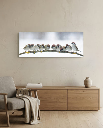 Sparrow flock in snow glass wall art above a low wood sideboard beside a gray armchair