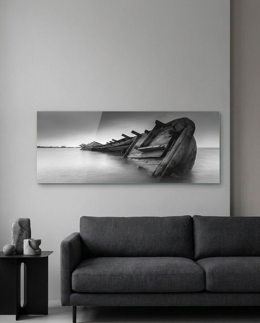 Black and white shipwreck panoramic glass wall art above a charcoal sofa on a pale gray wall