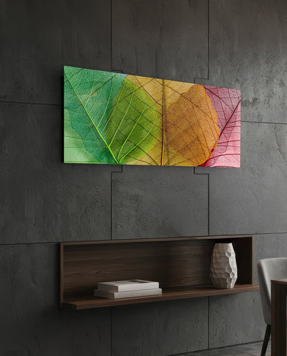 Green to pink veined leaves glass wall art on a dark slate wall above a walnut floating shelf