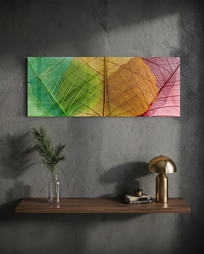 Green to pink veined leaves glass wall art above a floating shelf with a brass lamp and a plant in a vase