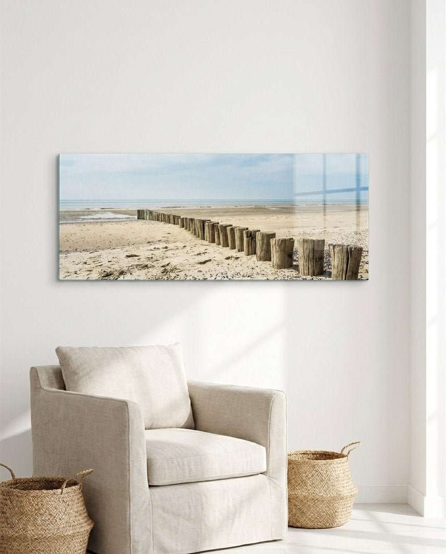 Weathered wood posts on the beach panoramic glass wall art above a cream armchair with woven baskets in a white room