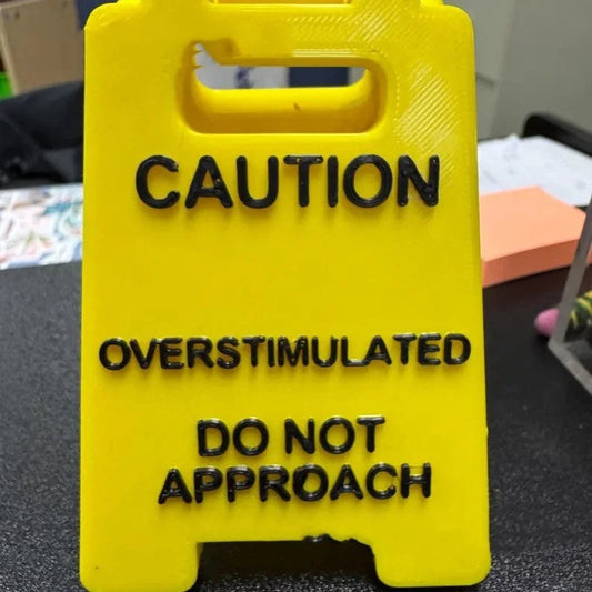 Close-up of the small overstimulated caution desk sign with raised lettering.