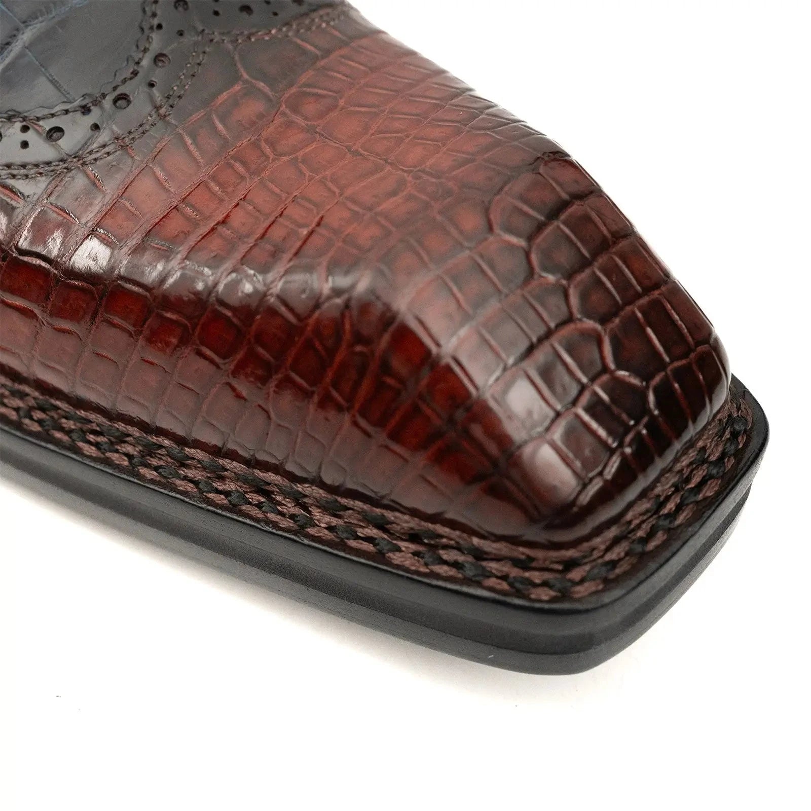 Close-up squared toe box crocodile leather shoes showing precision brogue perforations artisan craftsmanshipClose-up squared toe box crocodile leather shoes showing precision brogue perforations artisan craftsmanship
