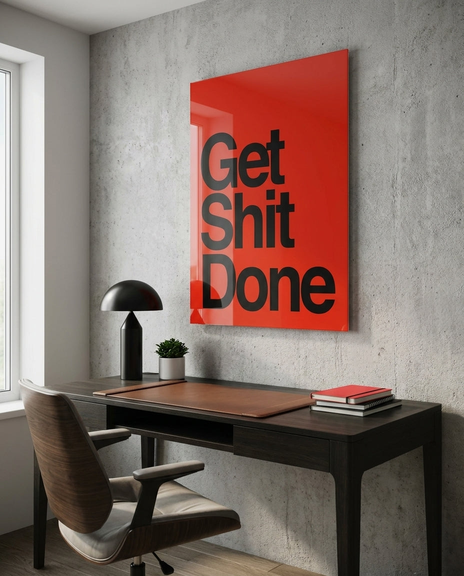 Get Sh*t Done bold black on red glass wall art on a concrete wall above a dark desk and lamp