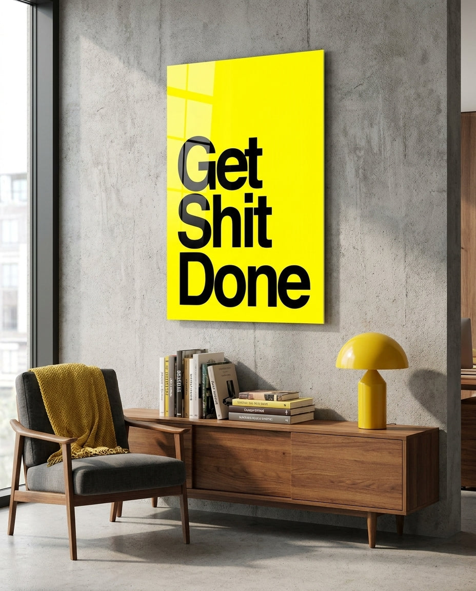 Get Sh*t Done bold black on yellow glass wall art above a wood sideboard with books and a yellow lamp