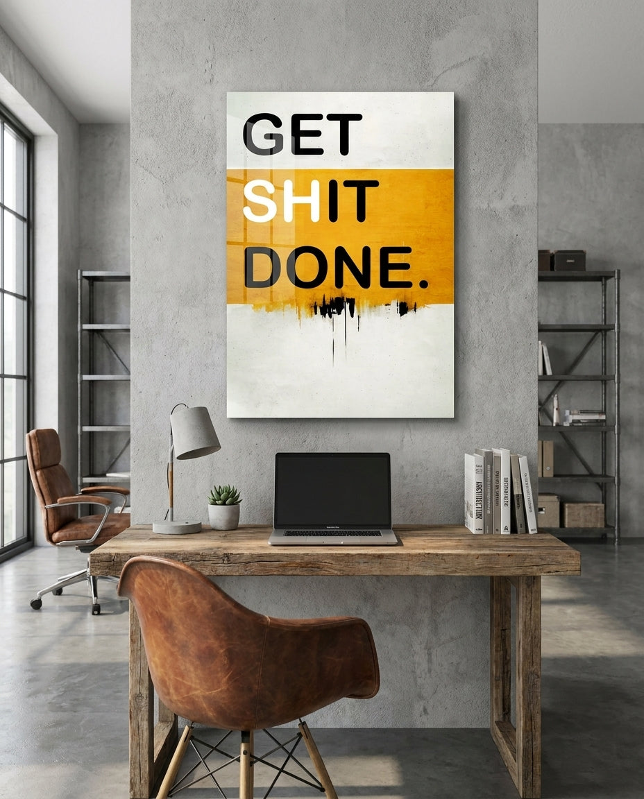 Get Sh*t Done mustard yellow glass wall art above a rustic wooden desk with a laptop and a brown leather chair