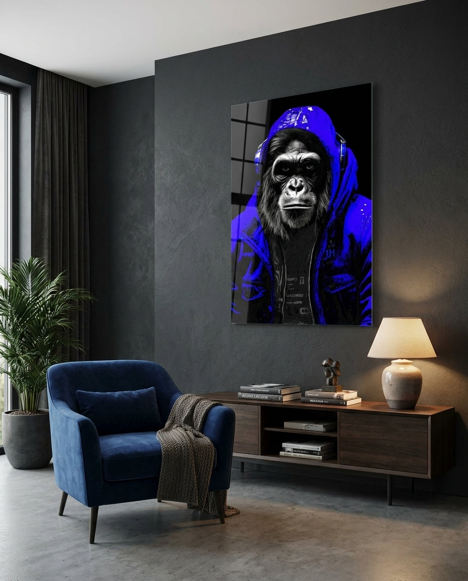 Gorilla in a blue hoodie glass wall art on a dark gray wall above a low sideboard beside a navy armchair