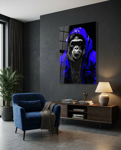Gorilla in a blue hoodie glass wall art on a dark gray wall above a low sideboard beside a navy armchair