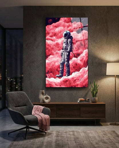 Astronaut in pink clouds glass wall art on a dark wall above a wooden sideboard beside a gray chair with a pink throw
