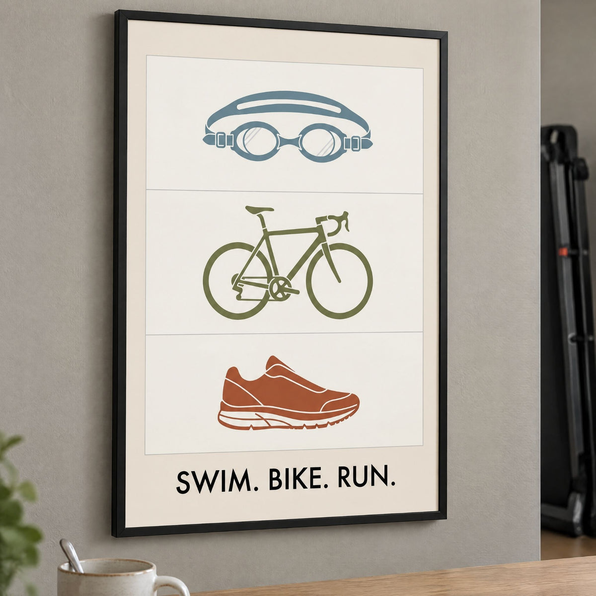 Framed triathlon icons print above an oak desk in a home office with a folded treadmill behind