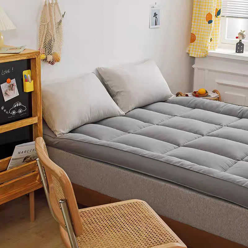 Grey mattress topper pad styled on bed with pillows in bright bedroom setting