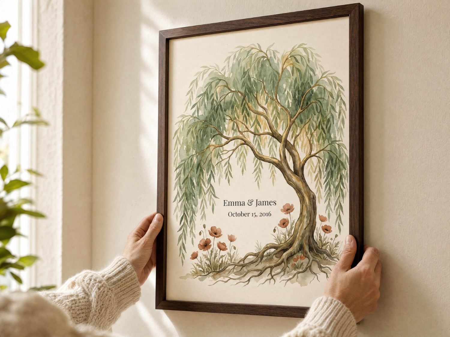 Hands hanging a personalized framed art print with names and date on a cream wall