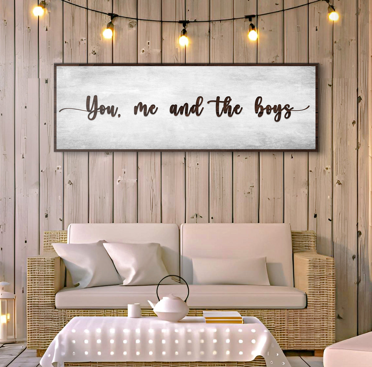 You, Me and the Boys gray canvas sign on a wood plank wall with string lights above a wicker loveseat