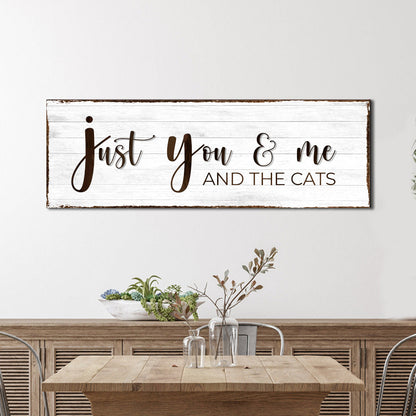 Long white wood-look canvas sign reading Just you and me and the cats in brown script, above a wooden console table