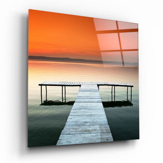 Orange sunset lake pier glass wall art on a white wall