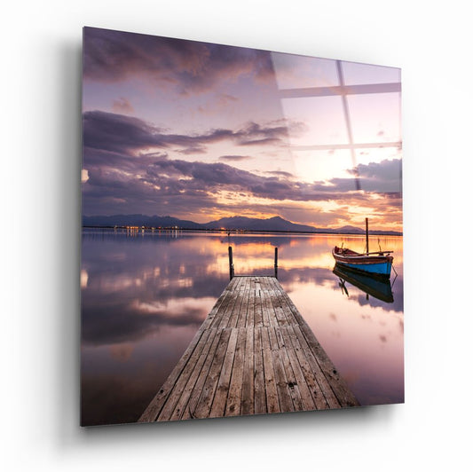 Dock glass wall art with a wooden dock over still water and a small boat at purple dusk