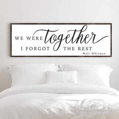 Wide white canvas sign with black calligraphy text: We were together, I forgot the rest, Walt Whitman, above a white bed