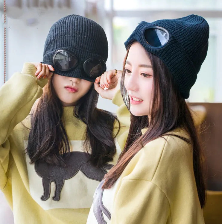 Models wearing black and grey knitted wool goggle hats, casual indoor styling
