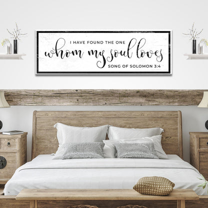 Long white canvas sign with a Song of Solomon 3:4 verse in bold curly black script and black bars top and bottom, above a bed