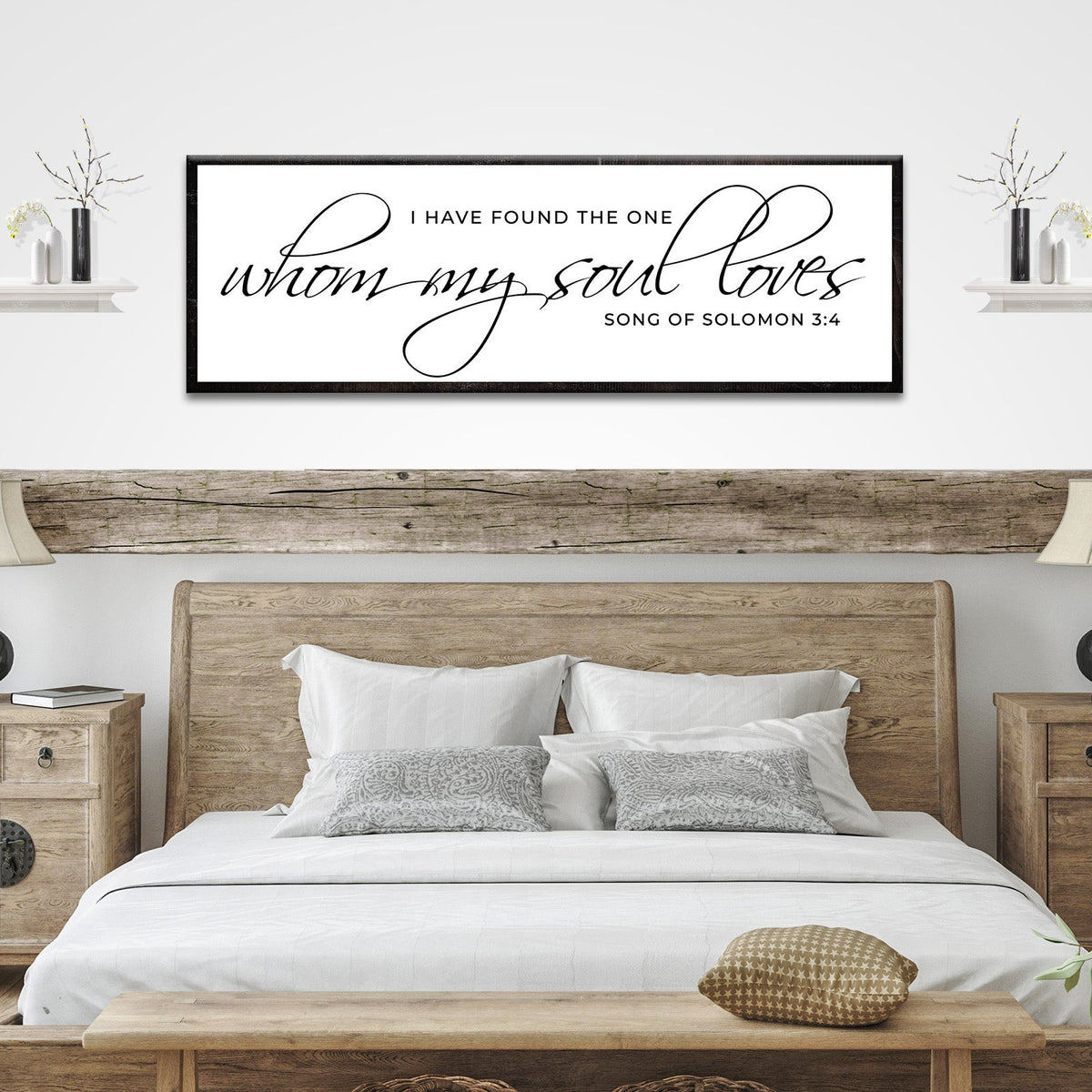 Long white canvas sign with a Song of Solomon 3:4 verse in thin flowing black script and a black border, above a bed