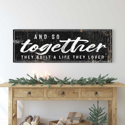 And So Together canvas sign in the black style with white brush script, above a wooden console with a pine garland