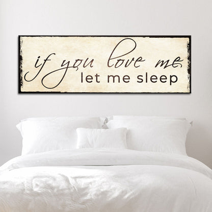 Long cream canvas sign with a let me sleep line in black script and a black edge, above a white bed